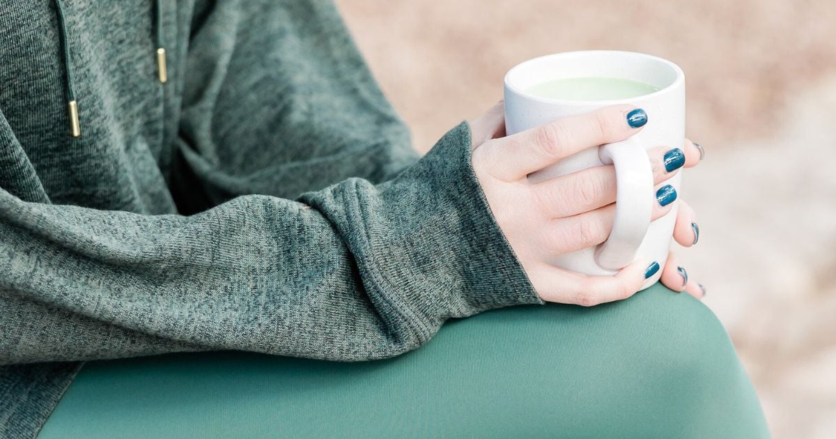 Lady in green workout clothes having a cup of tea outside