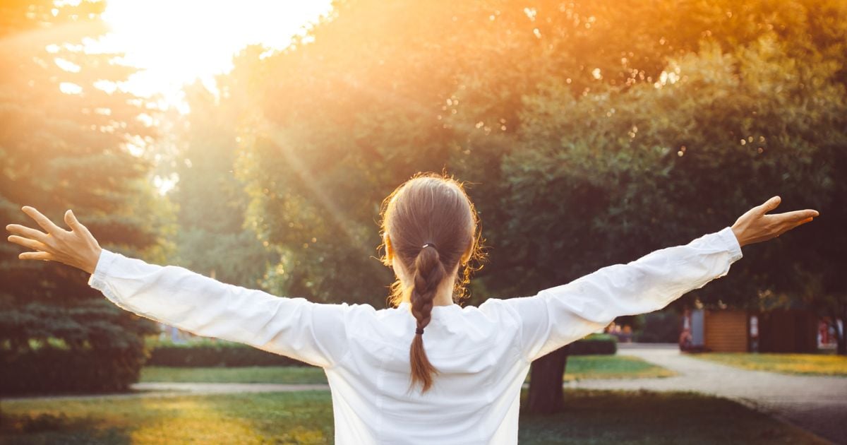 Lady in garden at sunset with her arms open looking at the sun like she's celebrating something, or feeling free