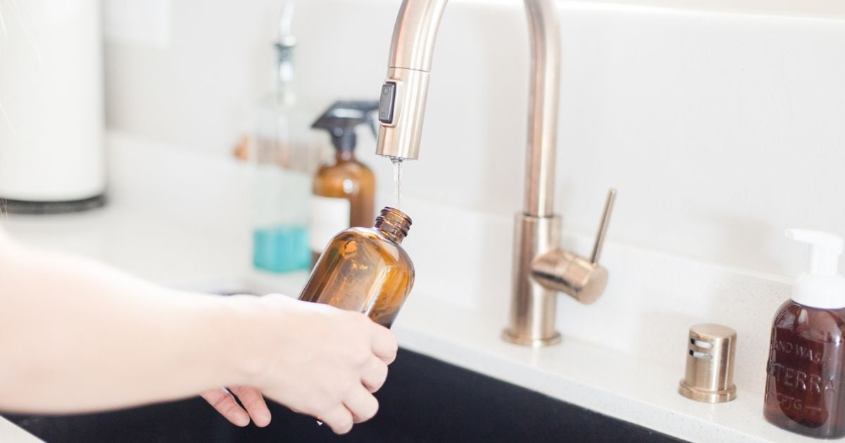 Hands filling up an amber cleaning bottle at the tap in a kitchen