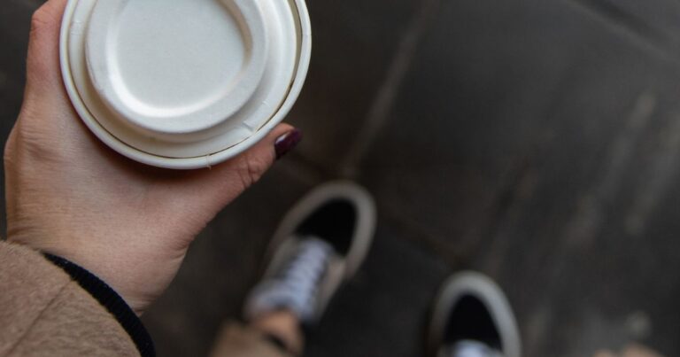 Hand holding a takeout coffee cup with a lid, from above - with trainers showing below