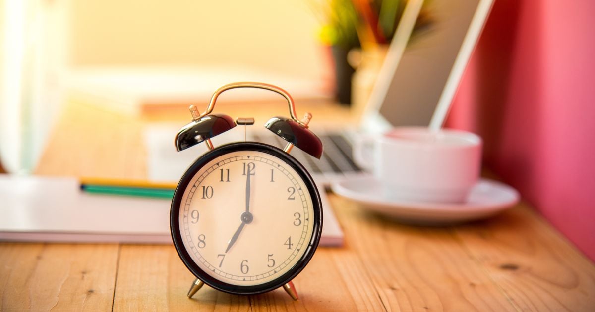 Black alarm clock on a desk with coffee cup in background