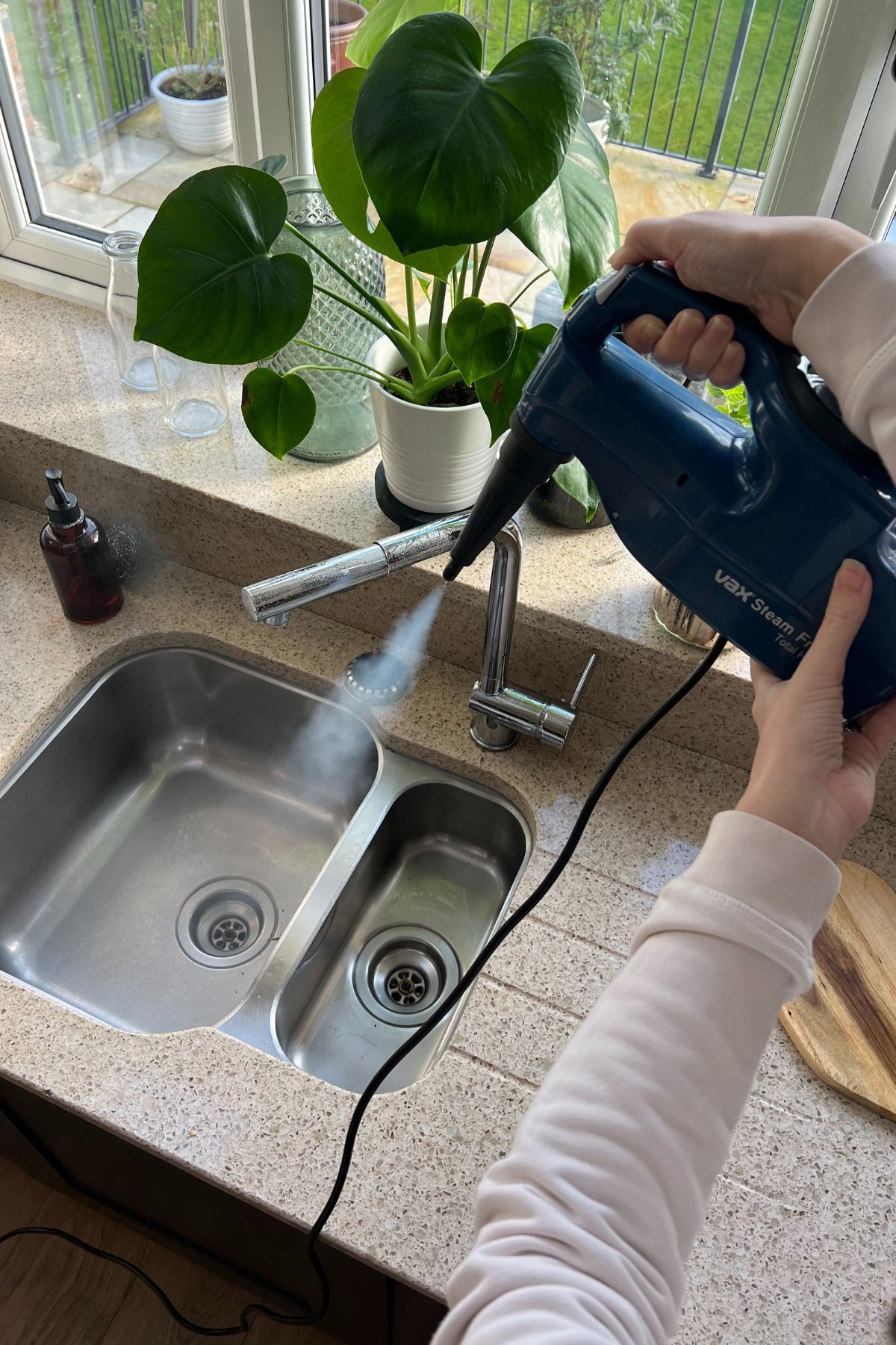Hand held steam cleaner being used for cleaning a kitchen sink and tap