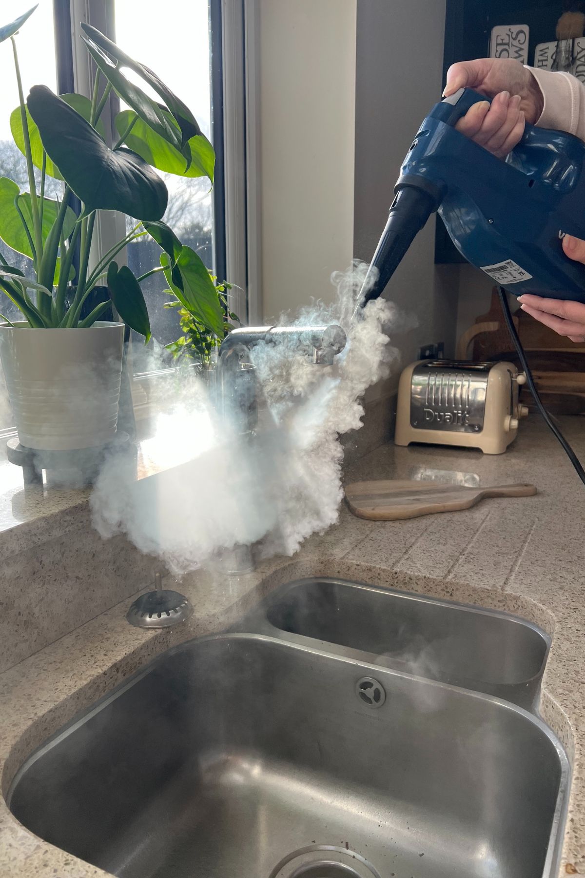 Hand held steam cleaner being used for cleaning a kitchen sink and tap