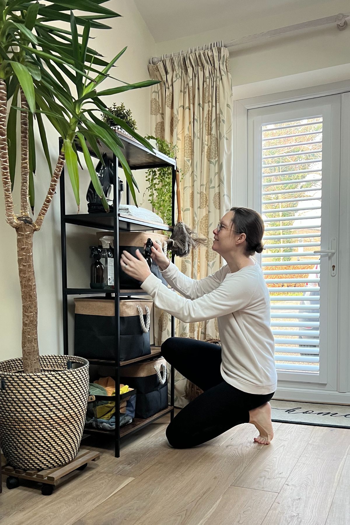 Shelving unit wood and black, with cleaning products in baskets and lady sorting them out