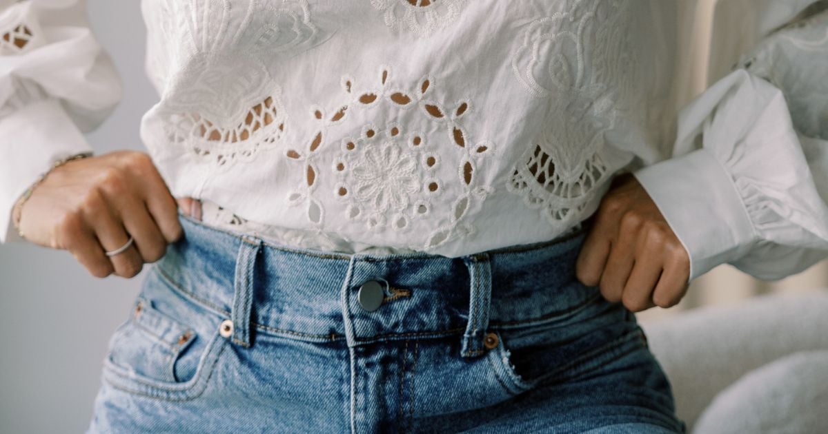 Lady with her hands on her sides, wearing blue jeans and a white top - closeup of waist area