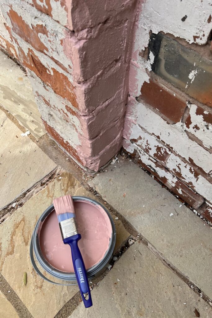 5 Budget-Friendly Steps to Creating a Spring Garden Space You'll Love 5 Ton of pink paint open with brush on top, against the base of a brick wall that's partly painted