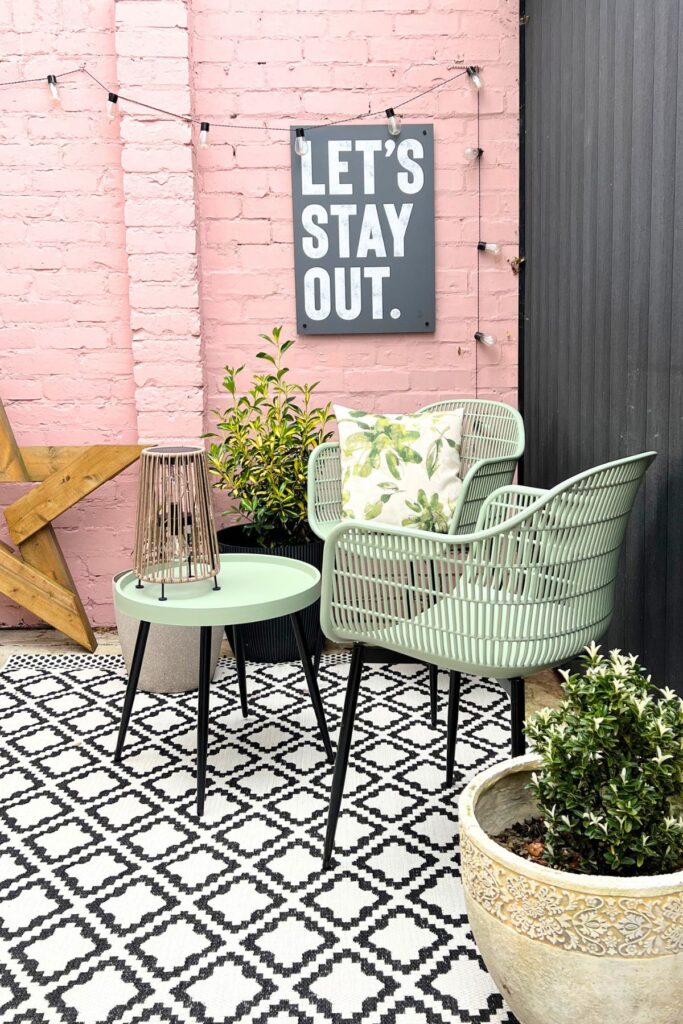 5 Budget-Friendly Steps to Creating a Spring Garden Space You'll Love 8 Spring Garden Glow Up of patio area with green seats, black and white outdoor rug, pink wall, and accessories