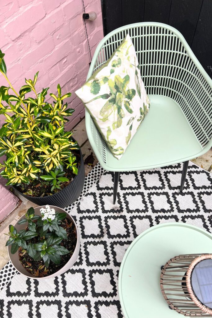 5 Budget-Friendly Steps to Creating a Spring Garden Space You'll Love 7 Closeup of Spring Garden Glow Up of patio area with green seats, black and white outdoor rug, pink wall, and accessories