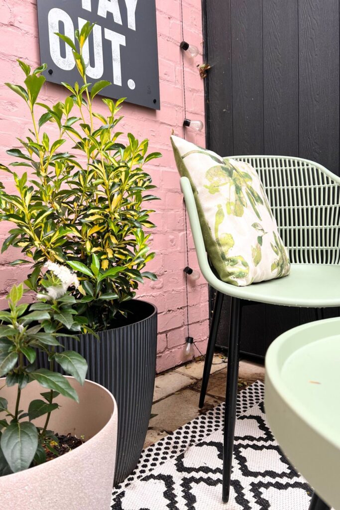 5 Budget-Friendly Steps to Creating a Spring Garden Space You'll Love 9 Closeup of area of garden patio makeover - green chair and table and pink wall with pot plants