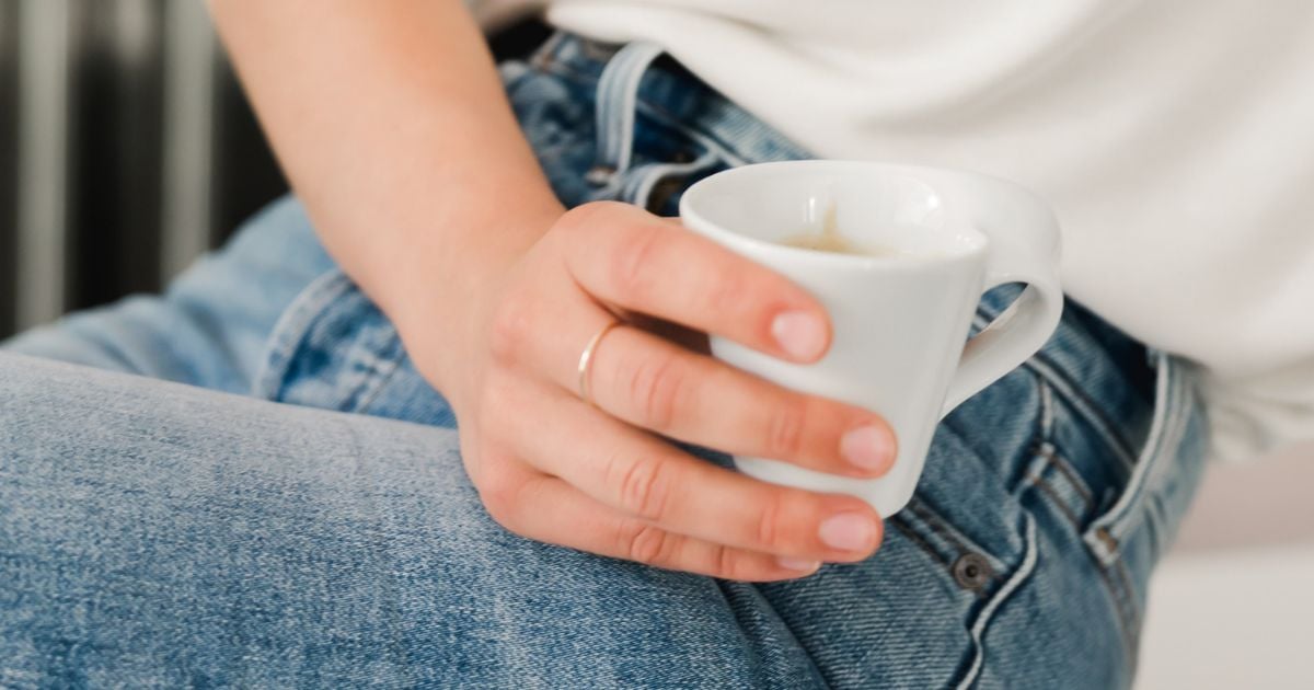 Lady wearing white top and blue jeans holding a white cup and sitting down
