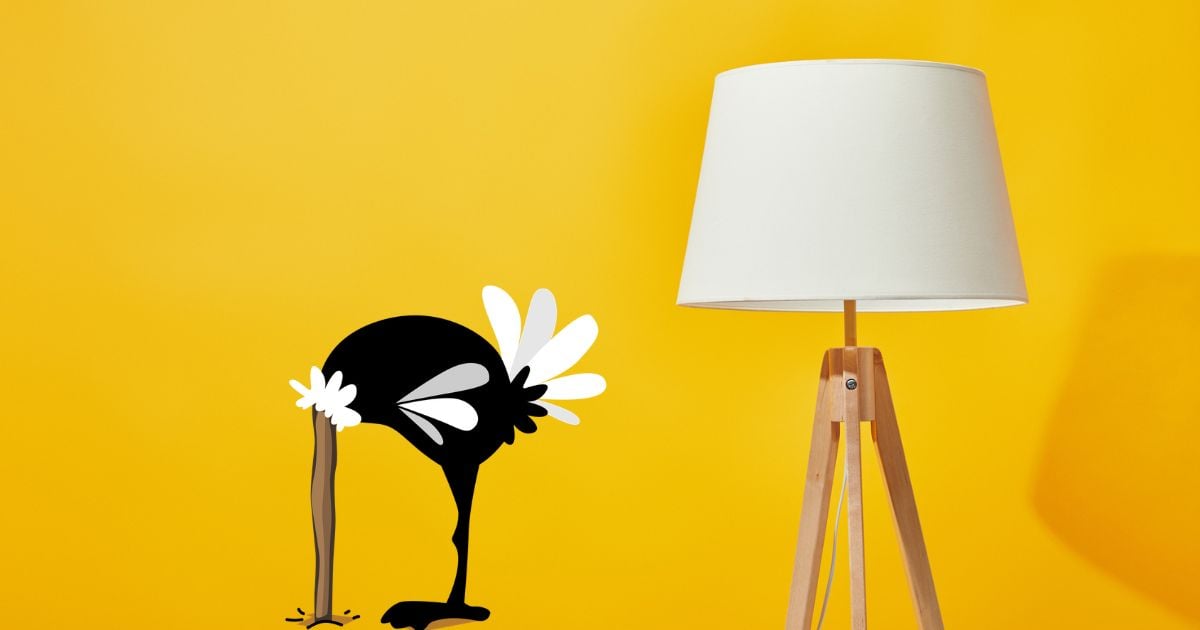 Ostrich with head in sand next to a lamp with a yellow background