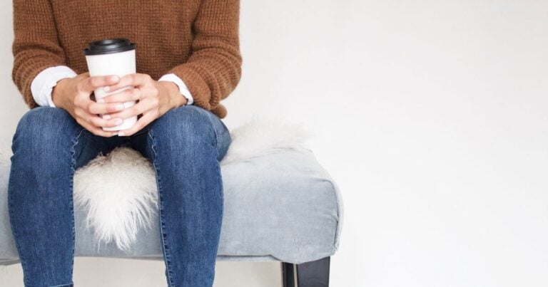 lady in jeans and a brown top with coffee in her hand sitting down