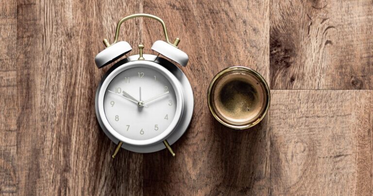 Alarm clock on it's side and cup of coffee from above on a wooden surface