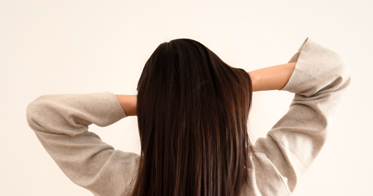 Lady with long dark hair looking away from the camera with her hands on the back of her head under her hair