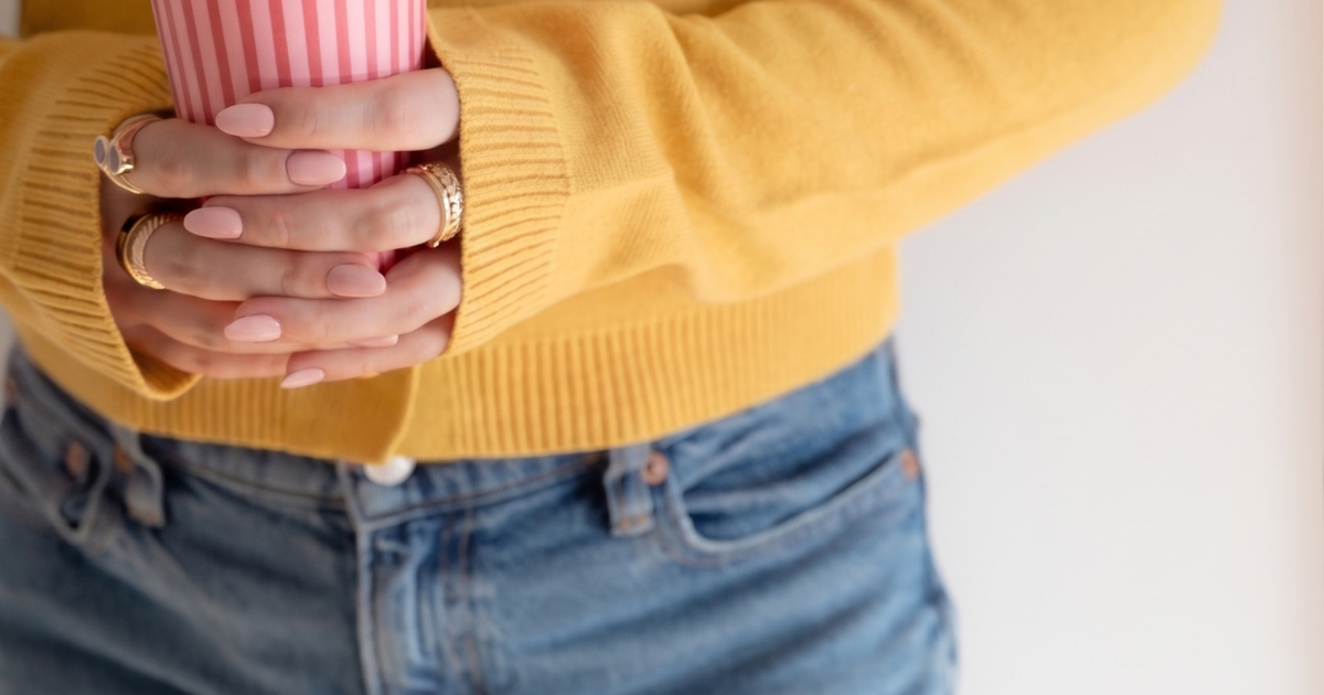 Lady in jeans and a yellow jumper holding a red striped takeout coffee cup
