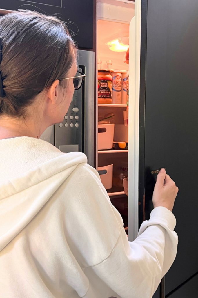 3 Simple Habits To Make Mornings Easier Every Day 5 Lady opening a fridge door in a black kitchen, ready to make a morning smoothie
